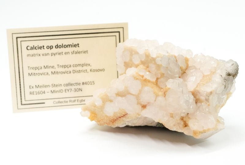 White calcite on cream-colored dolomite crystals from the Trepča mine in Kosovo, alongside the accompanying label.