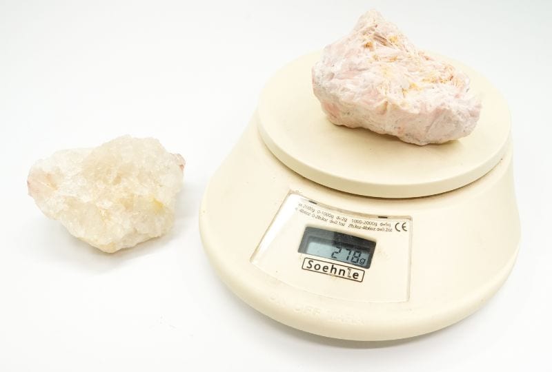 A 278-gram raw piece of barite on a scale next to a piece of quartz weighing 164 grams, which is about the same size.
