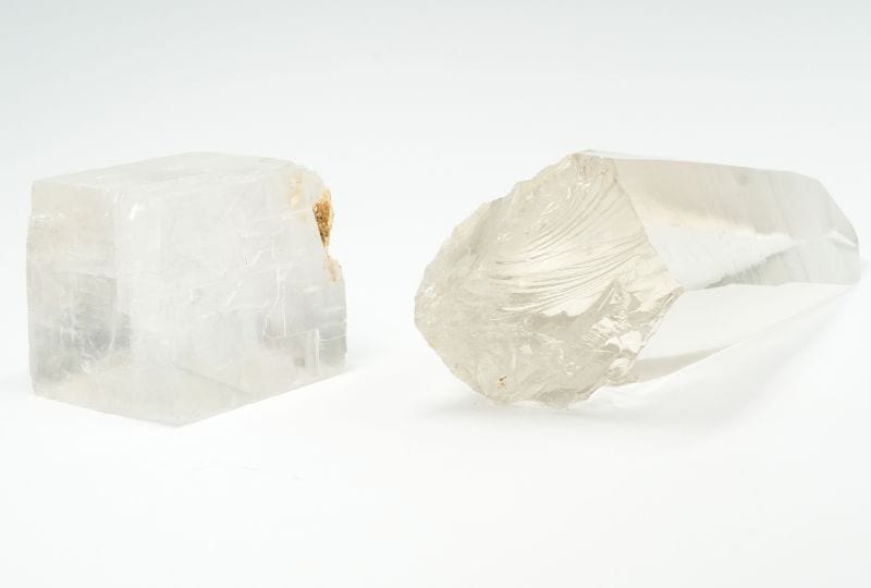 A calcite cleavage fragment next to a quartz crystal with a shell-shaped fracture.